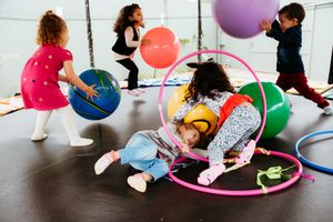Children holding colorful hula hoops participate in a recreational activity class in a bright indoor space.