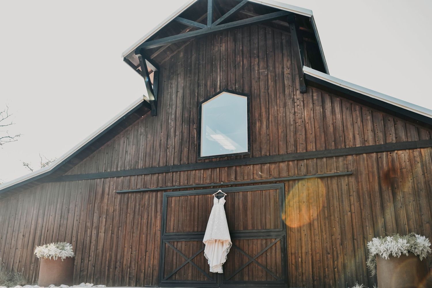 a lace bridal gown hangs on the rustic doors of the whispering oaks barn