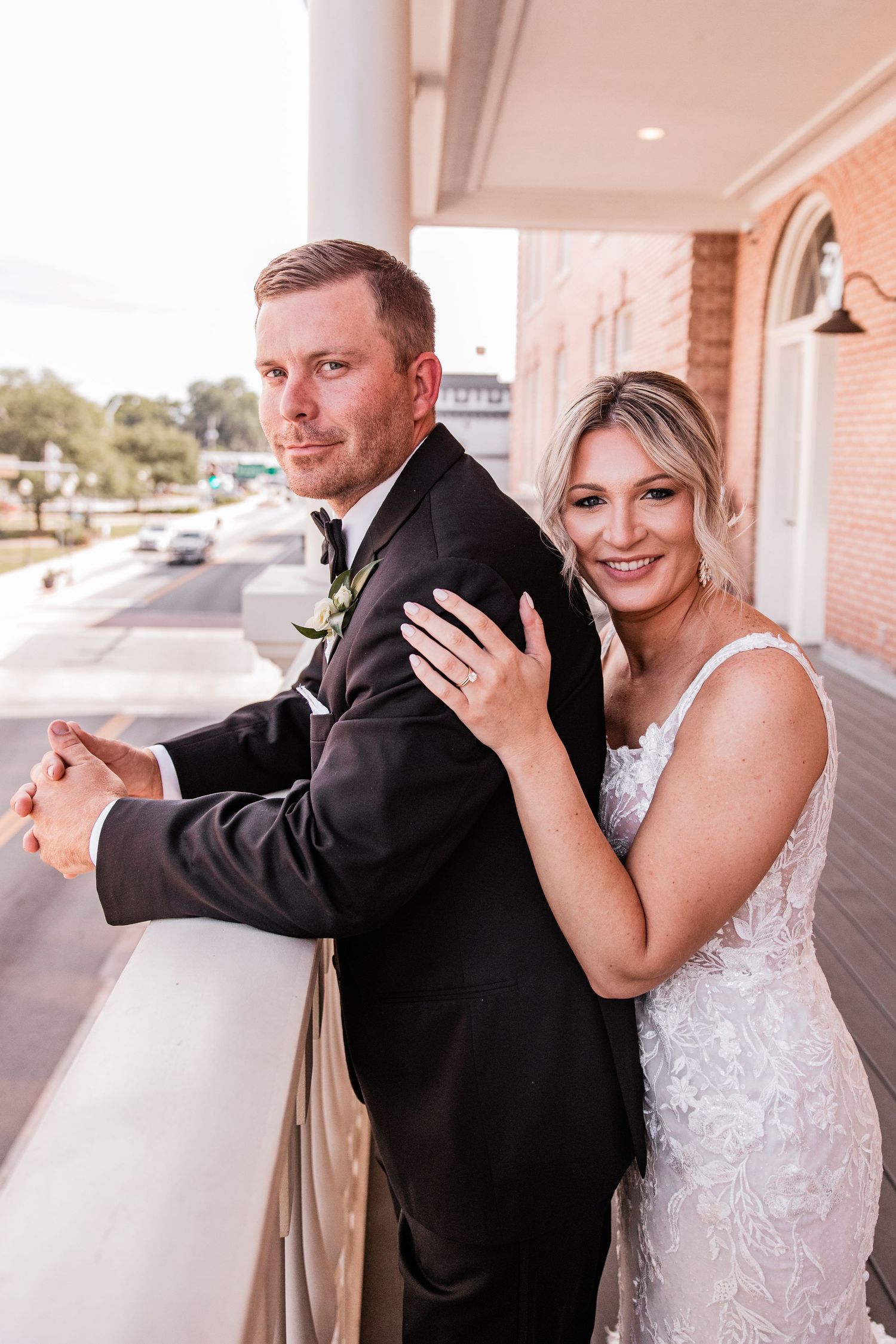 Playful wedding couple dances and poses along covered brick walkway.