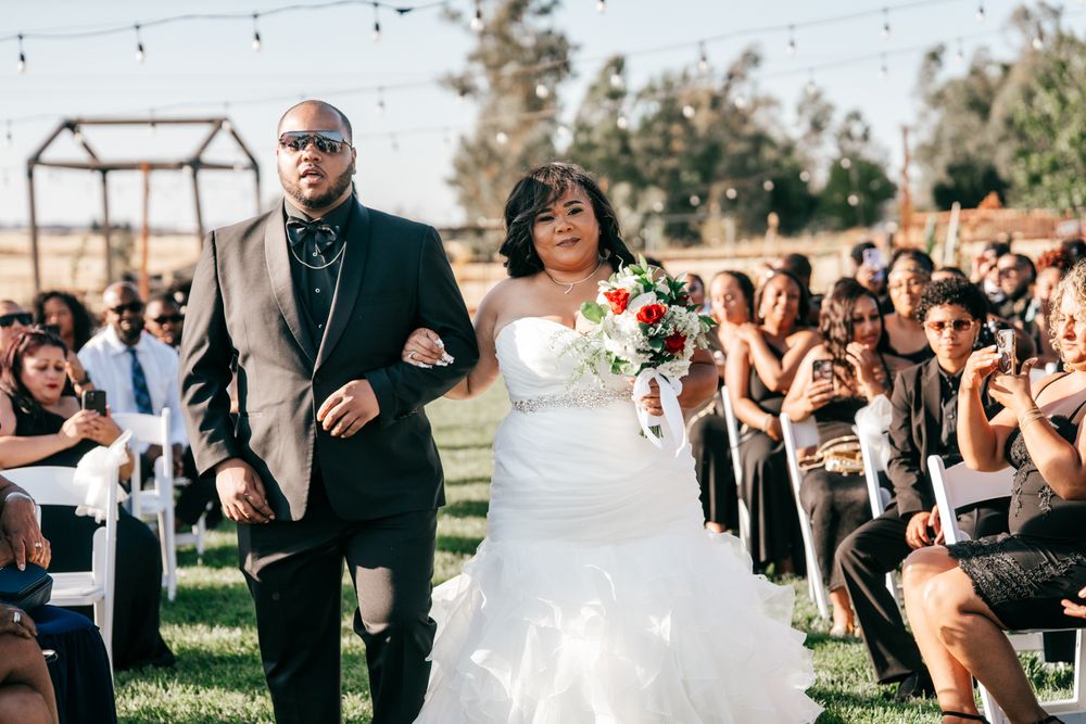 An outdoor wedding ceremony with a couple walking down the aisle as guests look on and take photos.