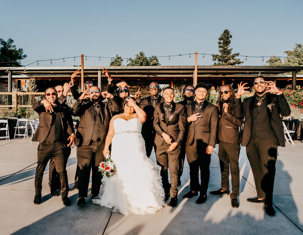 Fun wedding party portrait showing groomsmen in brown suits leaning back with bride on outdoor deck.