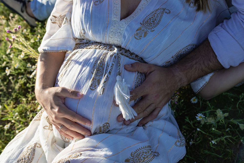 Woman in a white and gold patterned dress walking through a garden on a sunny day.