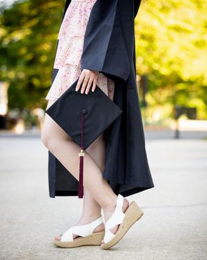 Close-up detail shots of graduation gown and white shoes during outdoor photo session.