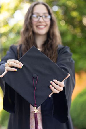 Creative graduation photo sequence showing hands holding and moving mortarboard cap against green background.