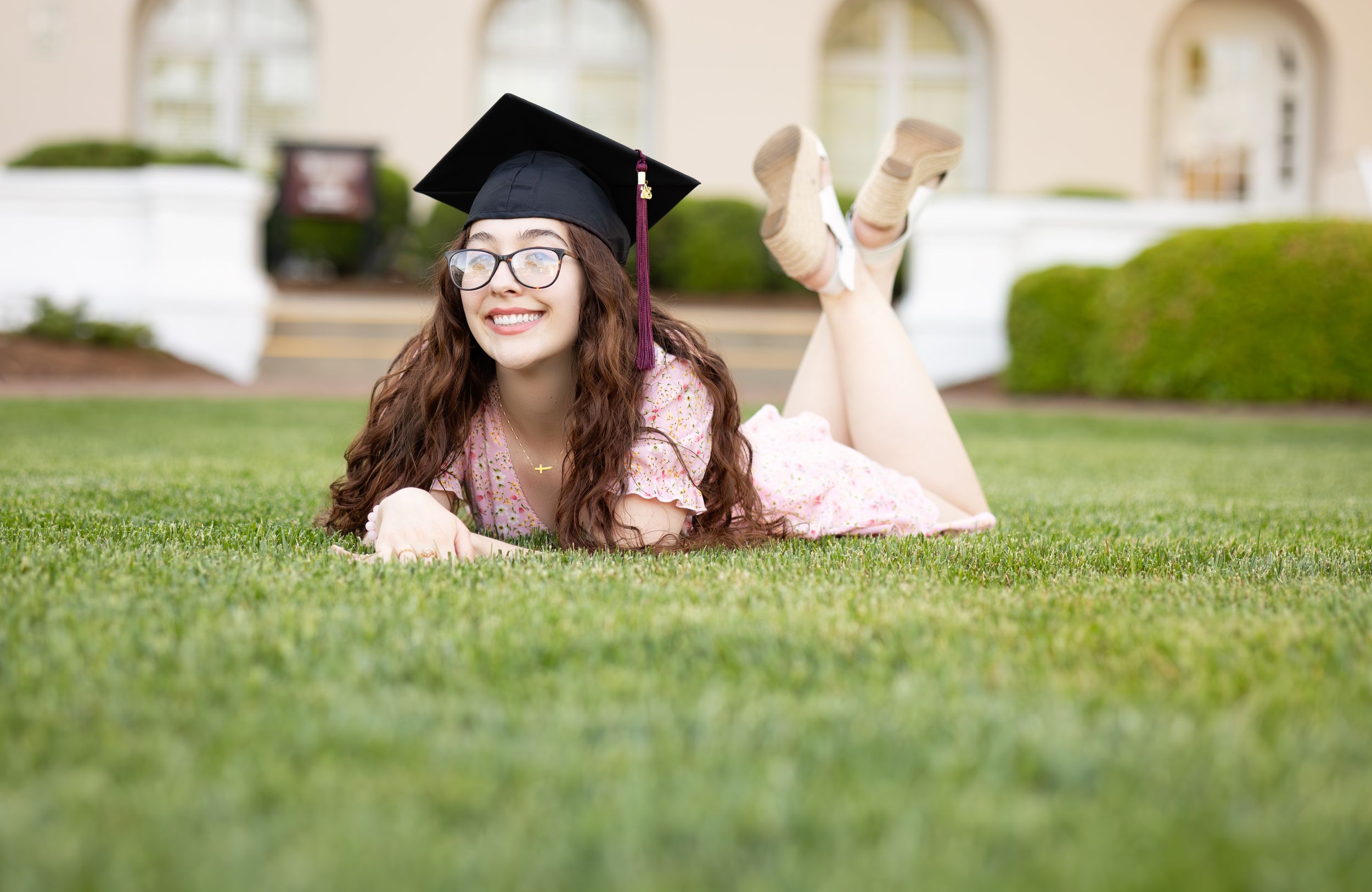 Graduation portrait session on green lawn showing graduate posing in cap and gown.