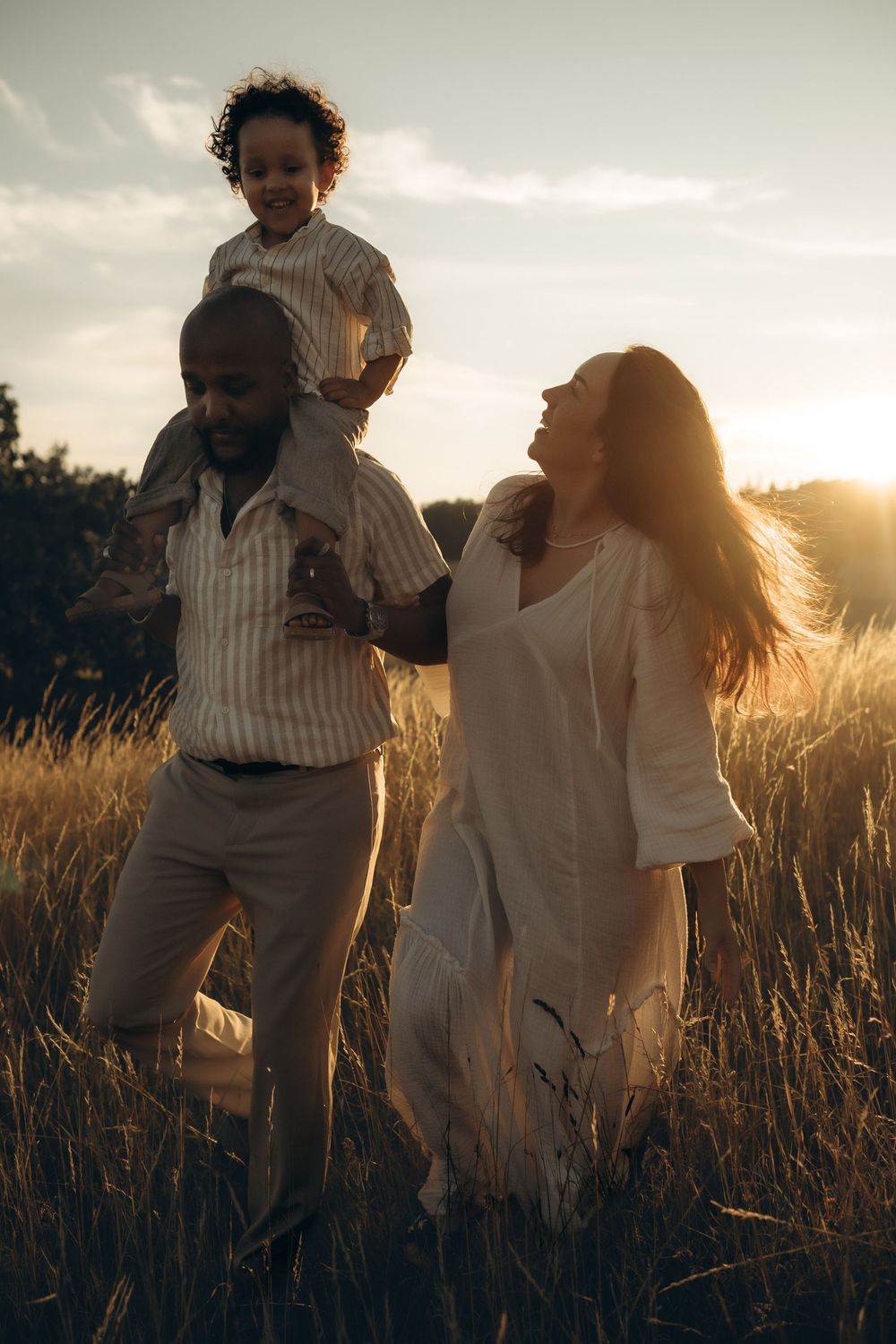 family walks through a field during sunset and laughs while being captured by documentary cinematic family photographer in Stockholm