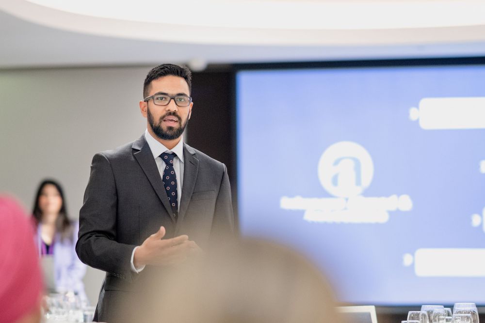 Professional presents during a business meeting with multiple screens and slides showing in a modern conference room.