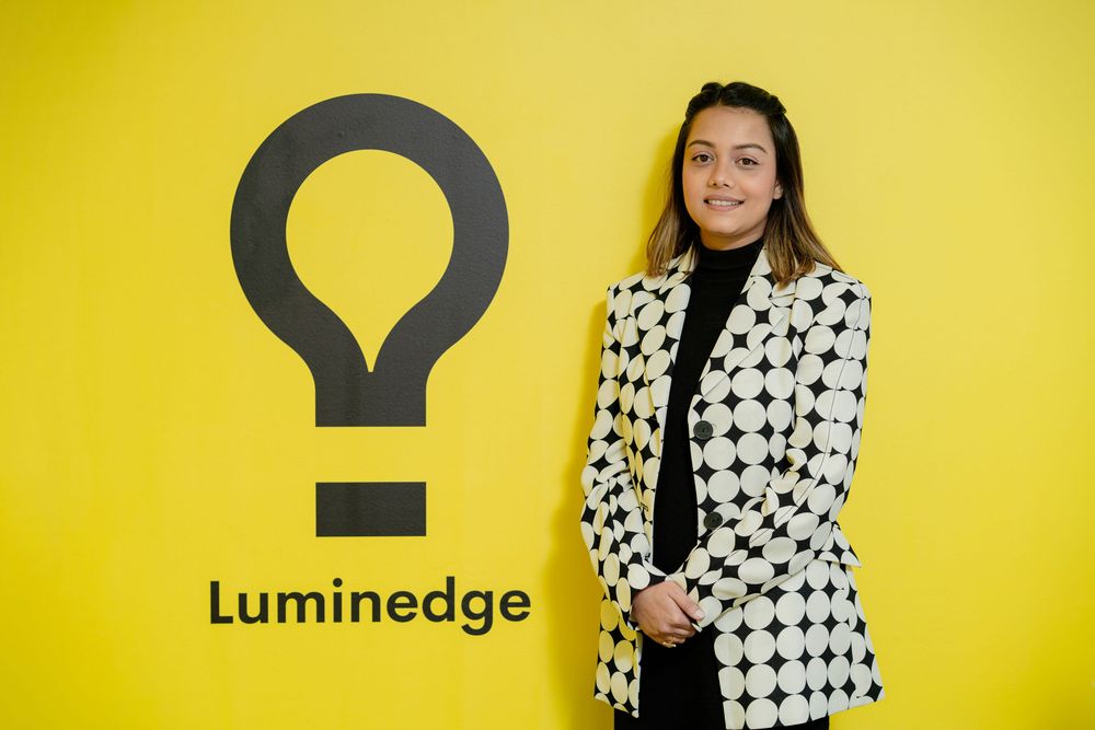 Professional model wearing a black and white houndstooth blazer against a bright yellow backdrop.
