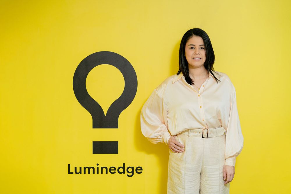 Person in white shirt gestures against vibrant yellow background showing upward arrow movement sign and business logo.