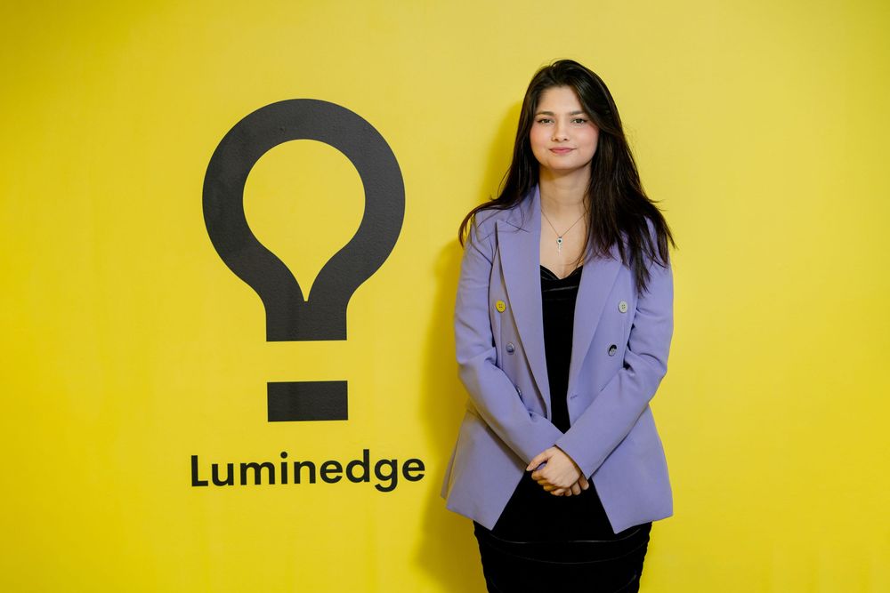 Person in a light purple blazer poses against vibrant yellow seamless background.