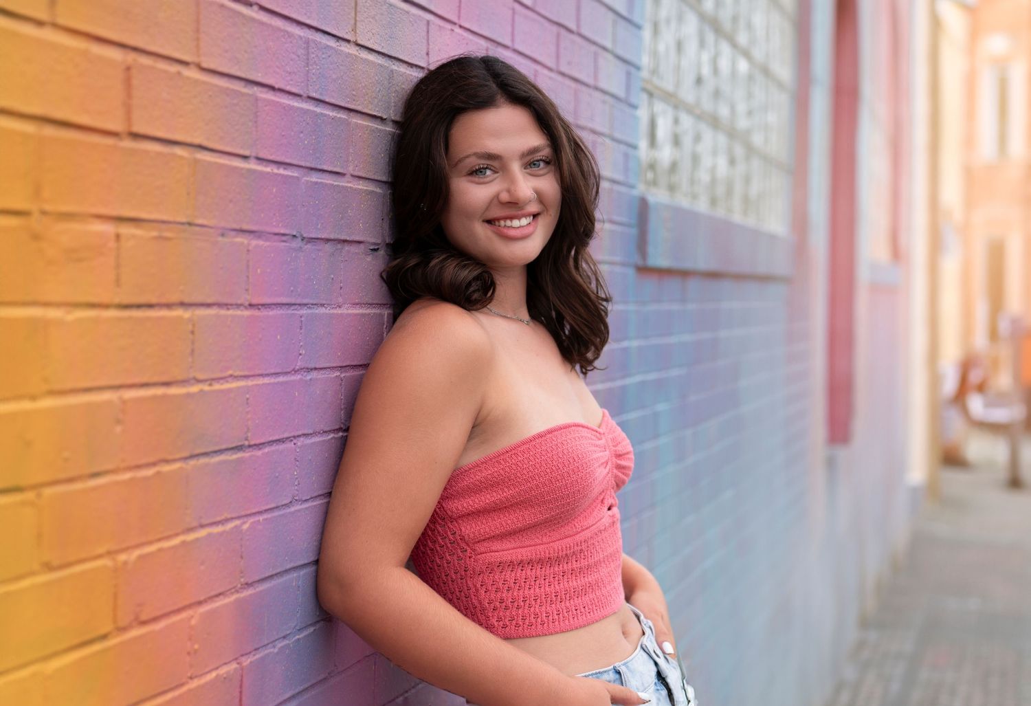 Person in a coral-colored dress poses for portraits against a brick wall with warm lighting effects.