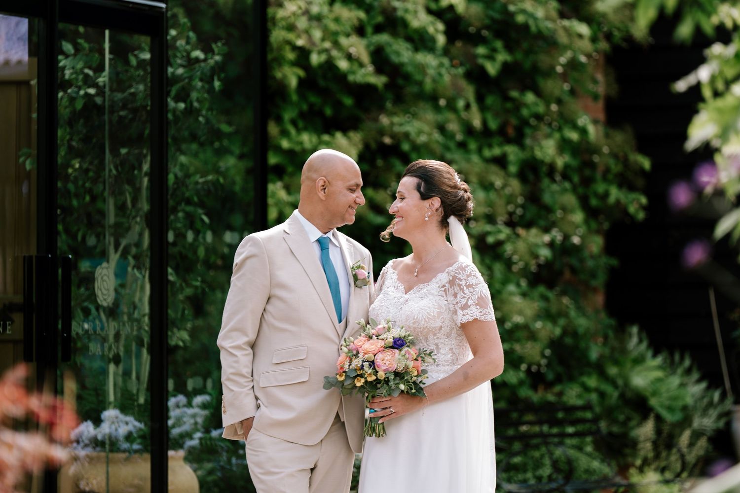 A happy newlywed couple shares a romantic moment in a lush garden setting at their summer outdoor wedding celebration.