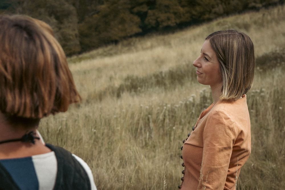 Author novel promotional photoshoot in Gloucestershire. Two people having a conversation in period costumes on a grassy hillside.