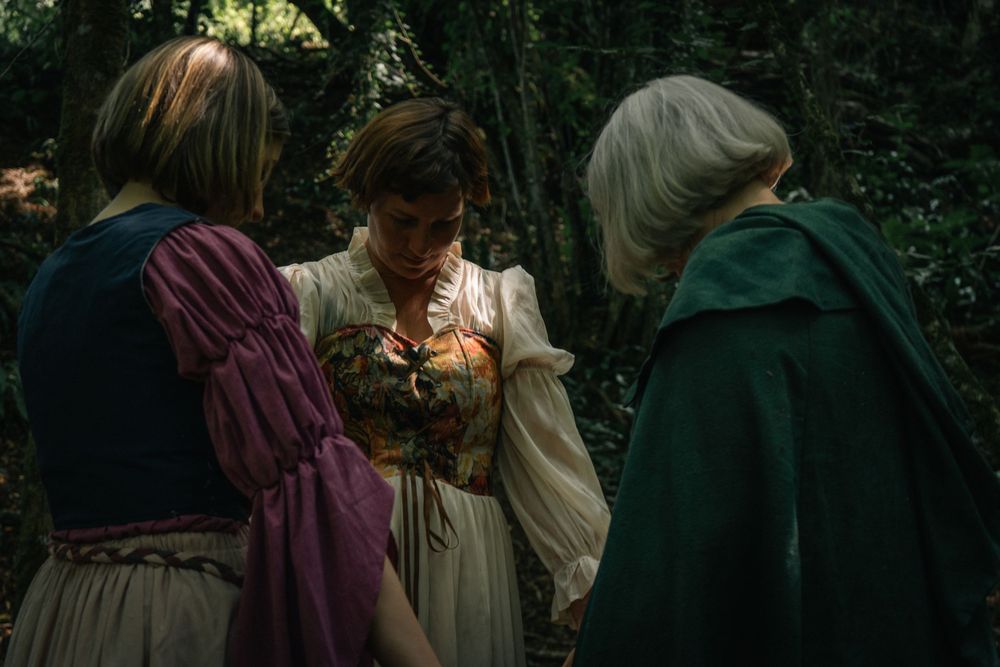 Author novel promotional photoshoot in Cotswolds. Period-costumed figures gathered in conversation along a wooded path.