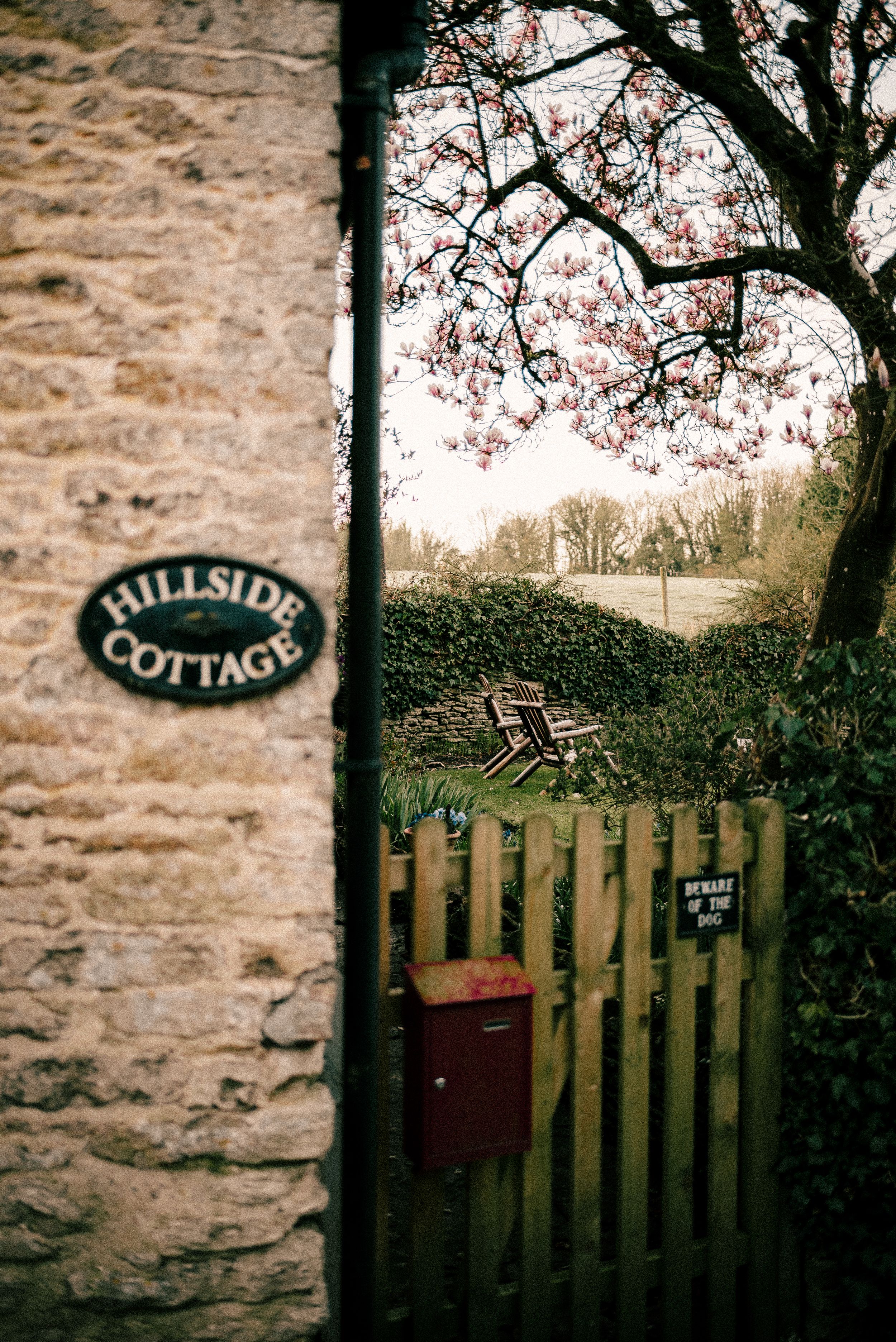 A rustic stone wall with wooden gates and ornate 'pub and dining' signage forms a charming entrance in a misty setting.