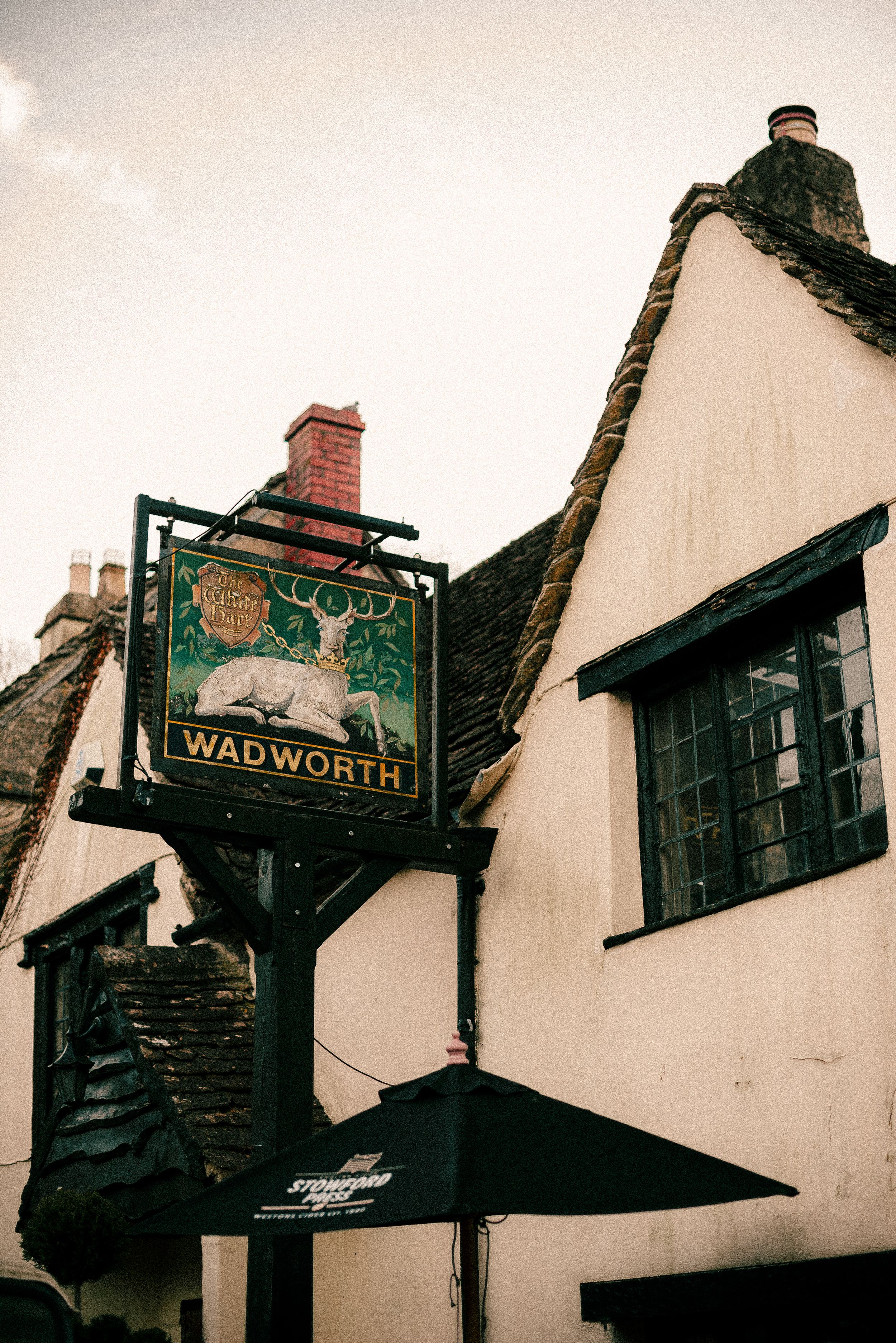Vintage pub sign for Wadworth brewery hanging outside a traditional white English building.