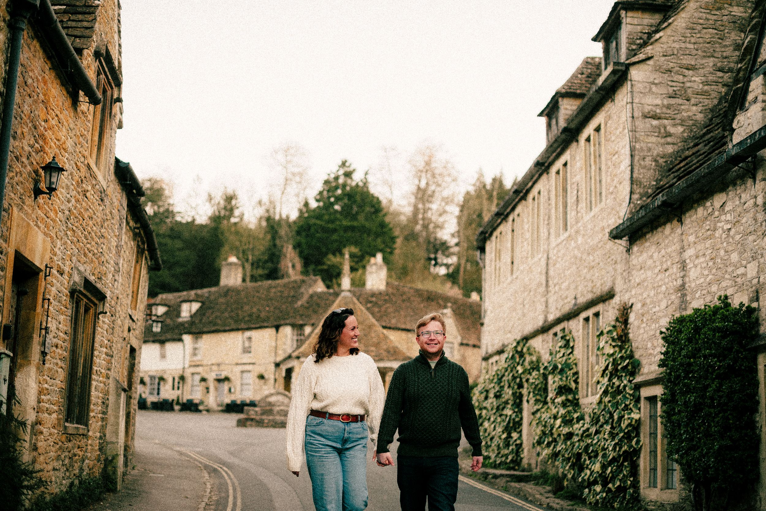 People walking down a charming stone-built village street with historic cottages in Castle Combe, Wiltshire.