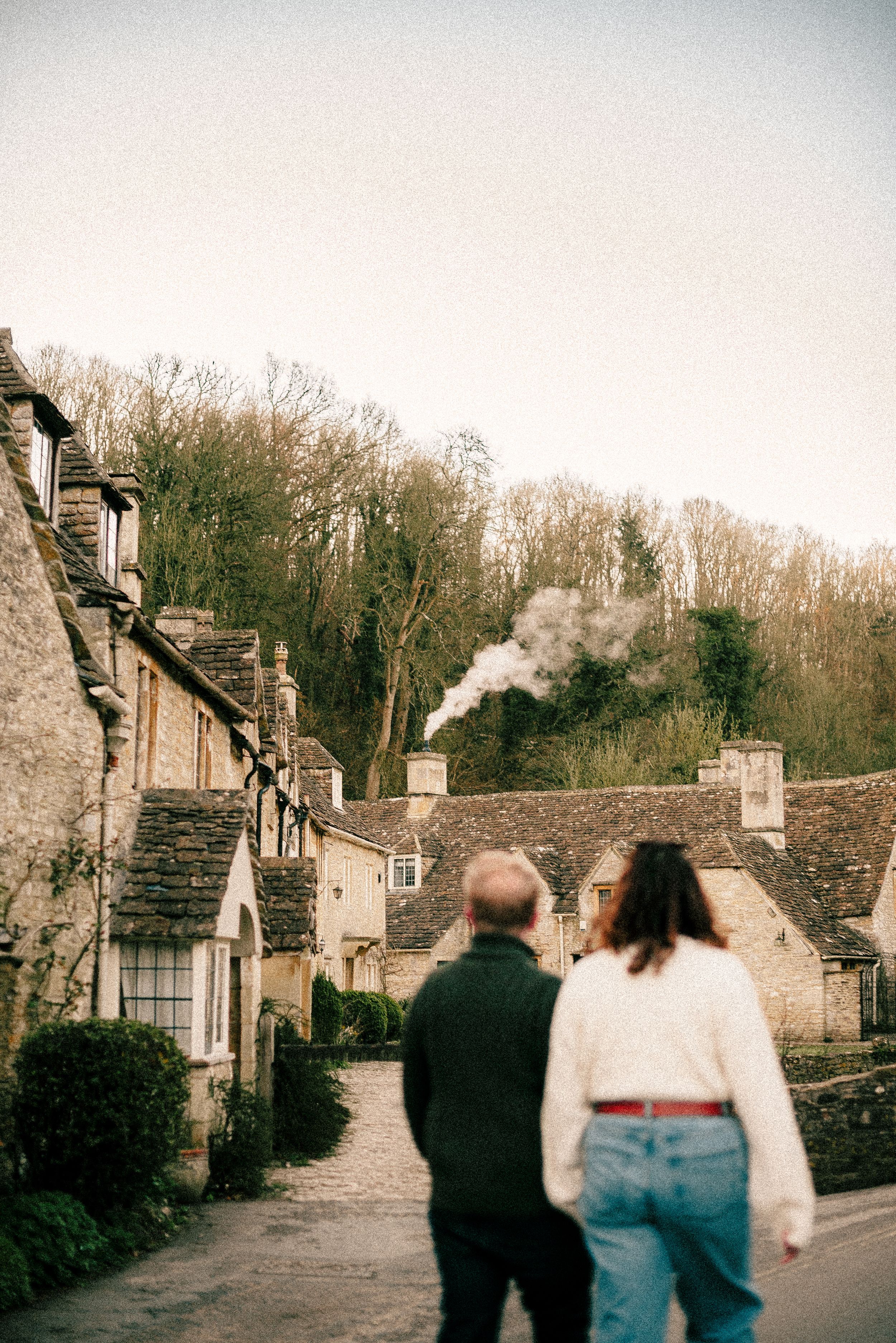 A row of connected vintage stone cottages on a rural street with figures walking in warm evening light.