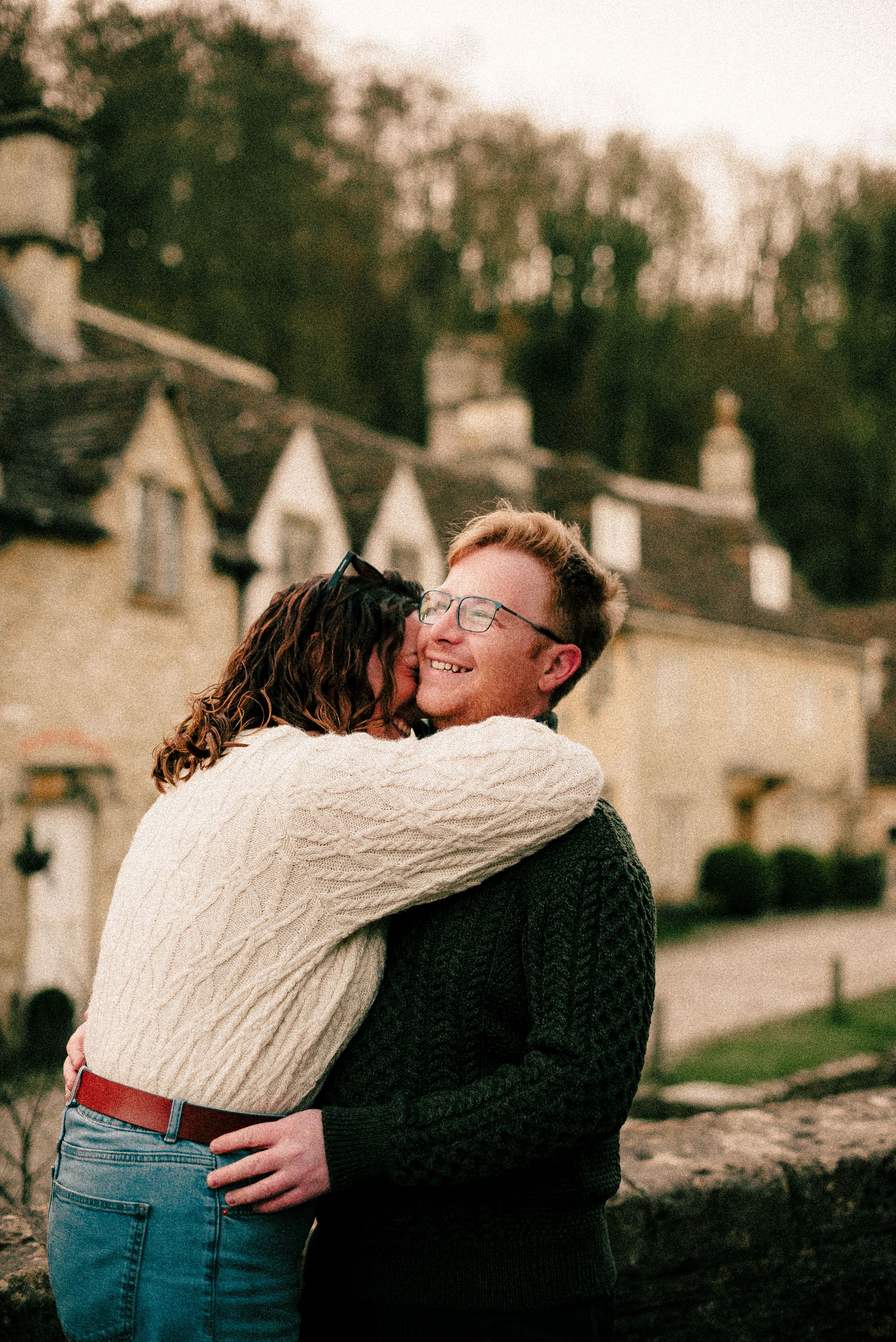A couple sharing a tender embrace against a rustic stone wall background in warm tones.