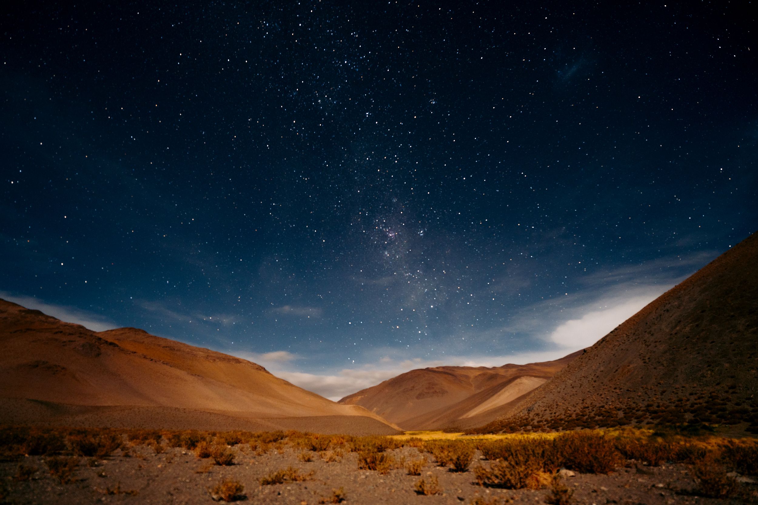 Star trails swirl over the Atacama Desert landscape as mountains and sand dunes stretch across the horizon at night.