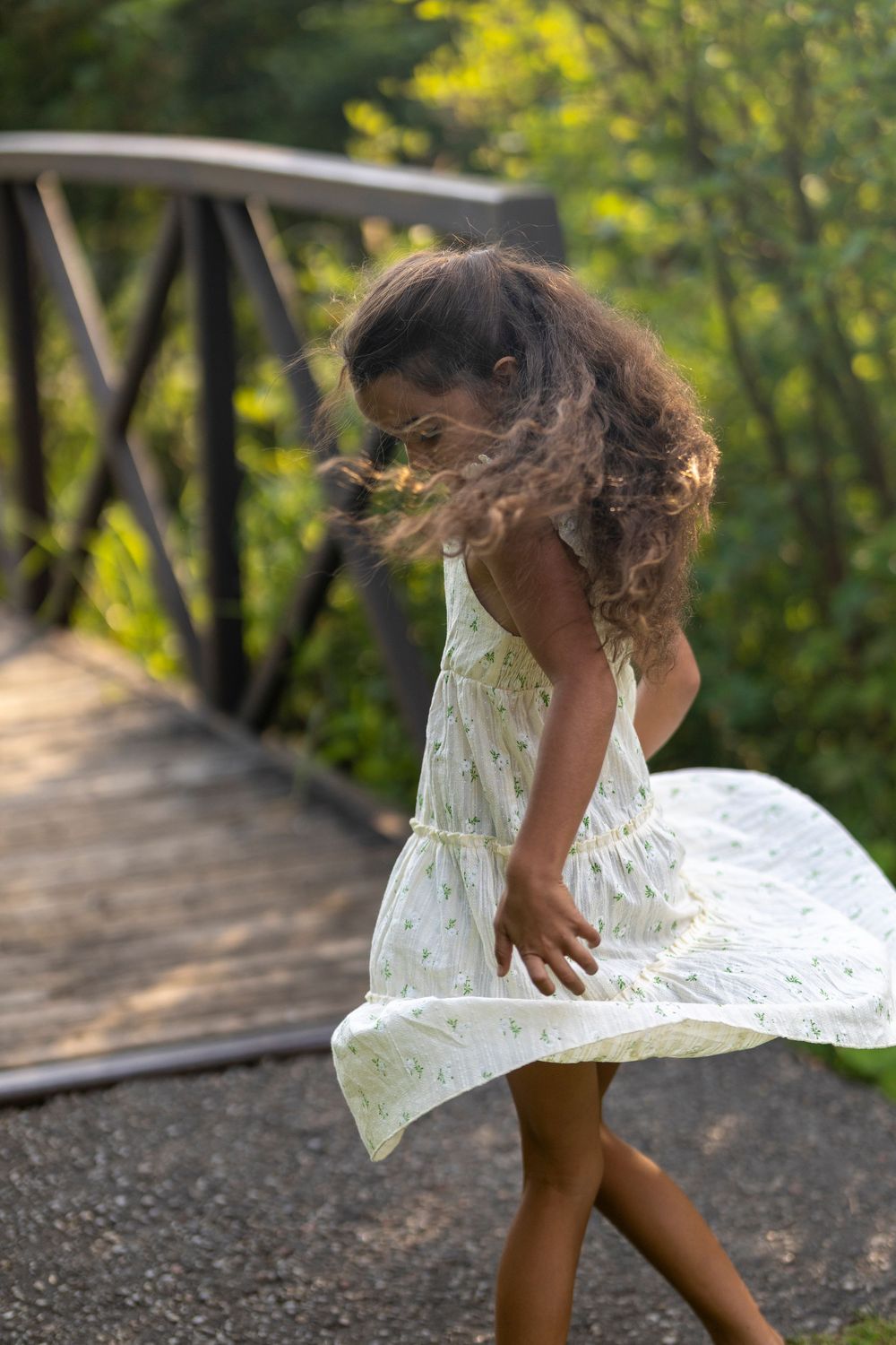A young girl twirling in her white dress infront of a bridge