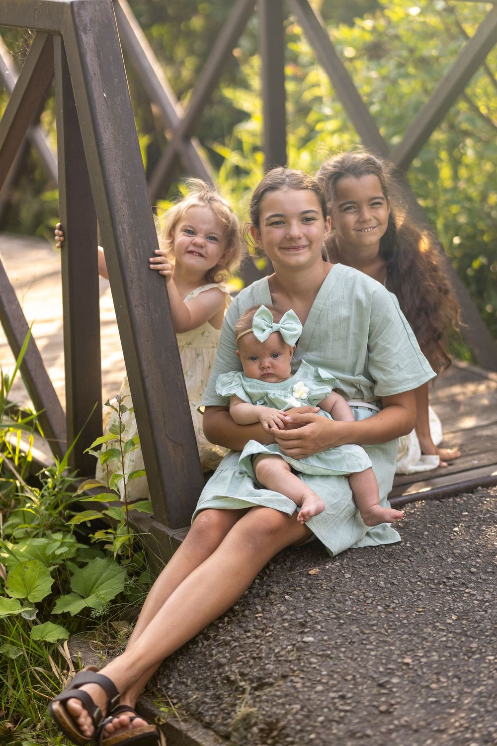 A group of four sisters sitting on a bridge with the oldest holding the baby sister