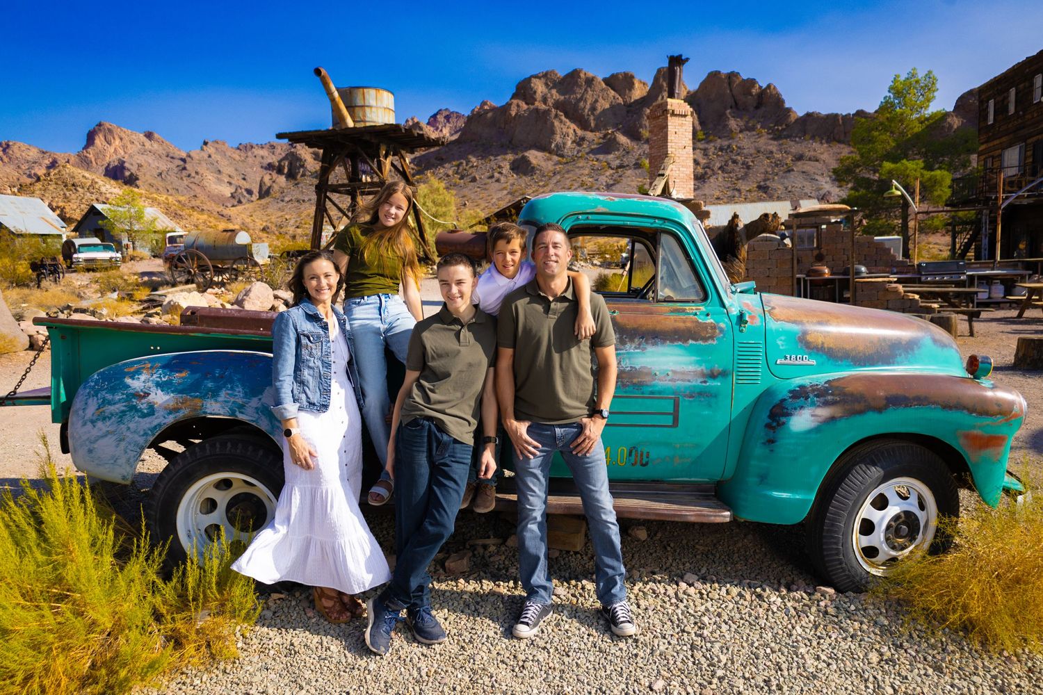 Vintage turquoise pickup truck parked in front of desert mountains with people gathered around it.