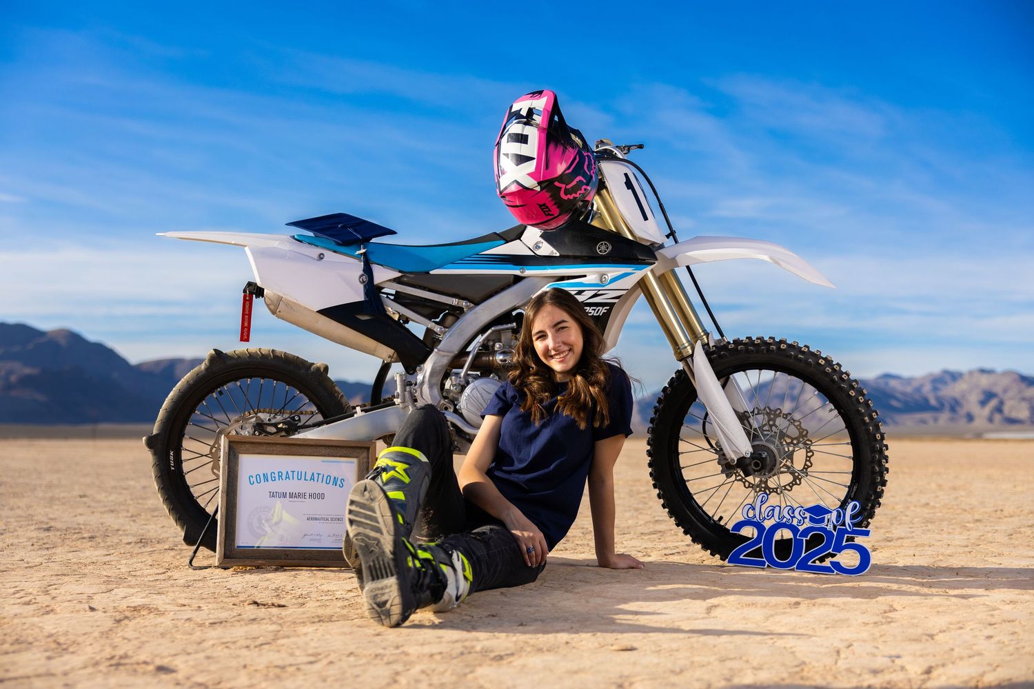 A high-performance dirt bike slides across desert terrain kicking up dust against a bright blue sky background.