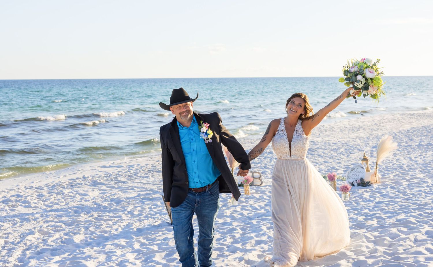 Joyful wedding couple celebrates while walking on white sand beach.