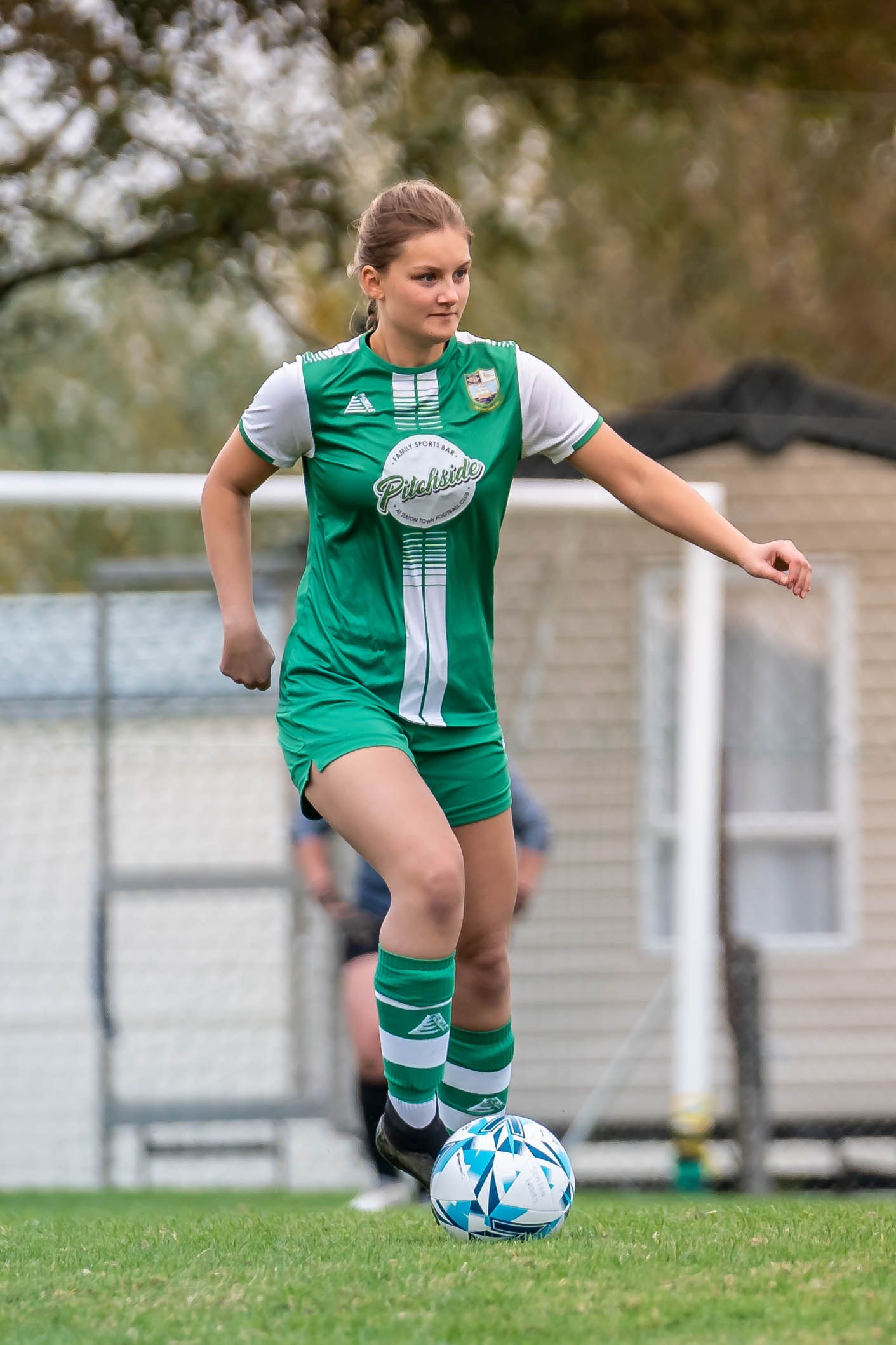 Soccer player in green and white uniform dribbling a ball during a match.