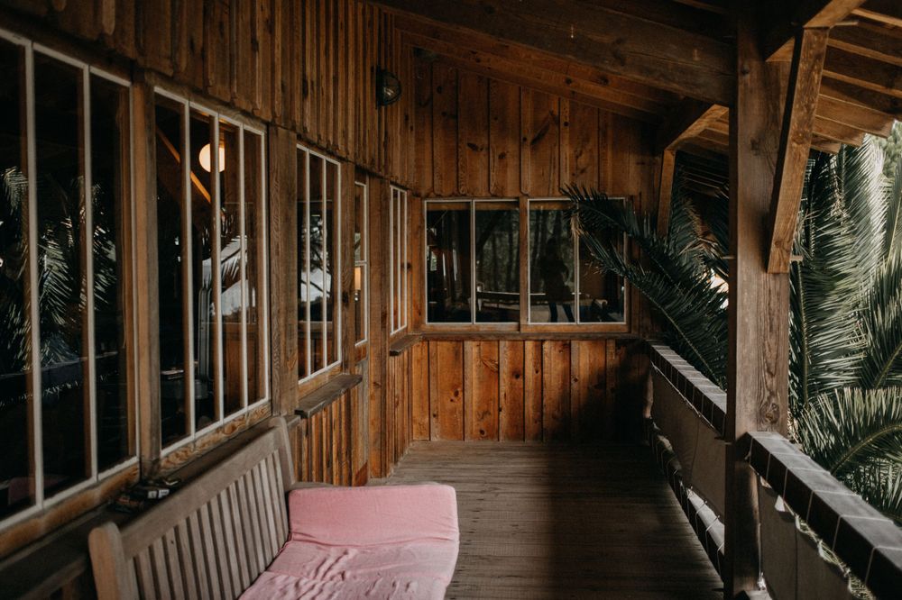 Wooden veranda with pink cushioned seating and large windows overlooking tropical foliage.