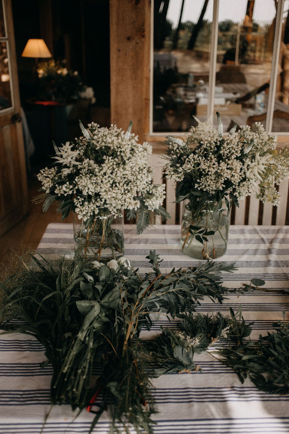 White floral arrangements in mason jars on a striped tablecloth create a rustic centerpiece display.