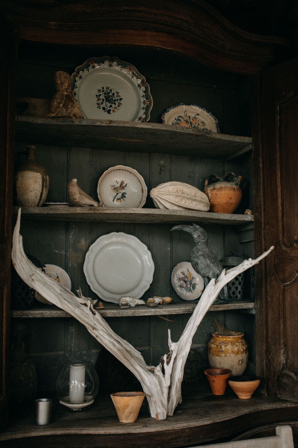 Vintage plates and decorative pottery displayed on rustic wooden shelves with driftwood accents.
