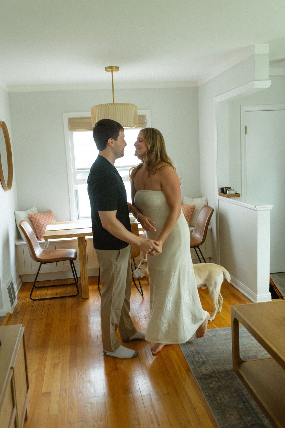 A couple in wedding attire practicing their first dance in a sunlit room with hardwood floors.