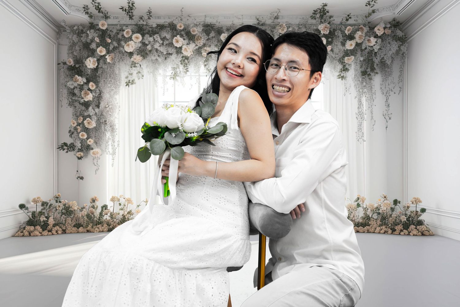 A couple poses together in an elegant white-themed setting with floral decorations.