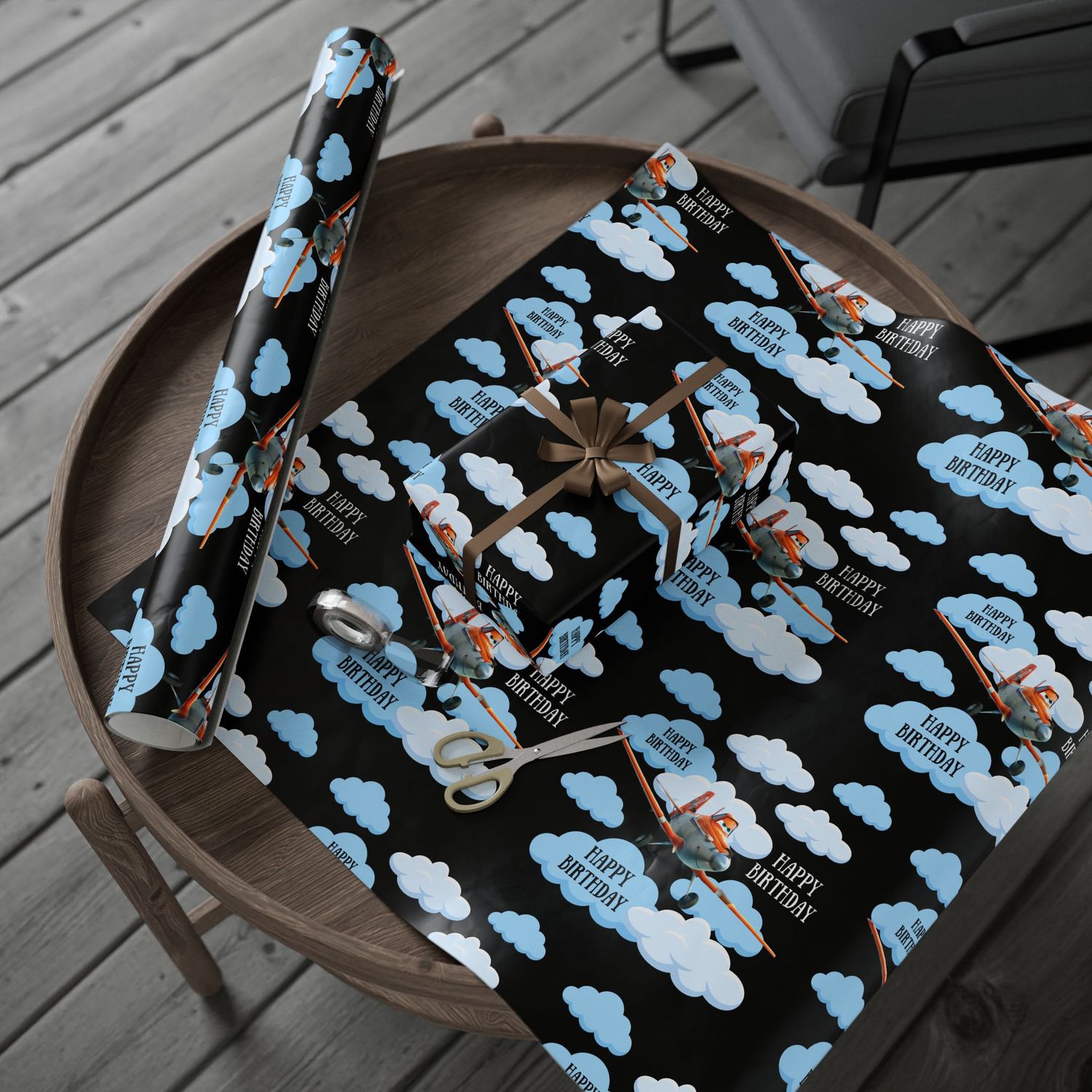 Gift wrap featuring blue clouds and orange planes displayed on wooden surface.