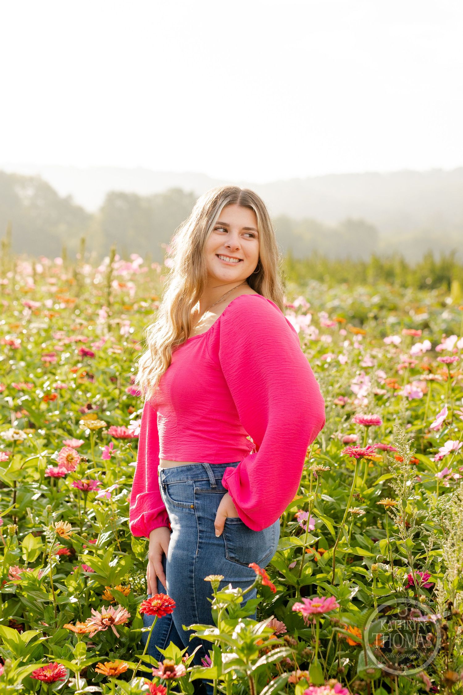A casual outdoor portrait among pink zinnias with mountains visible in the background.
