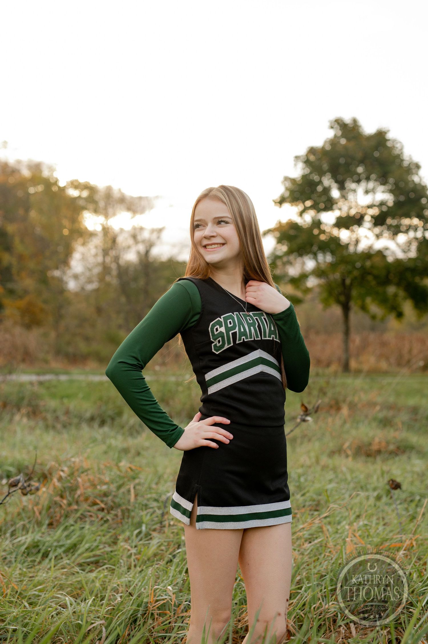 Cheerleader in Spartans uniform poses in grassy field during autumn season.