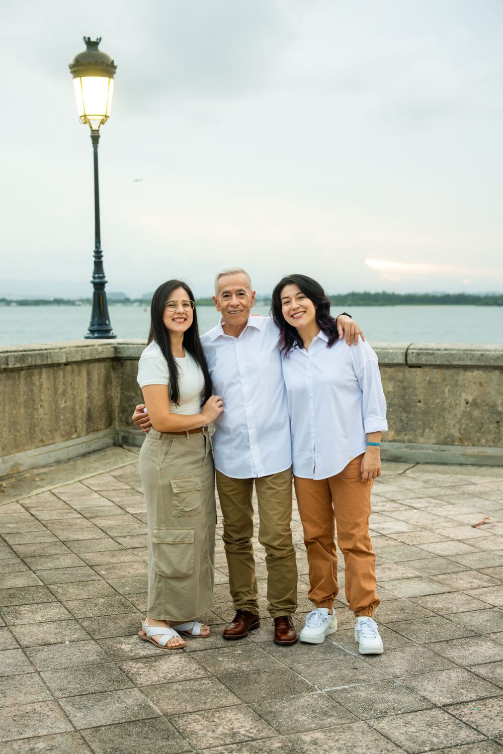 Three people in coordinated outfits posing by vintage lamppost near waterfront.