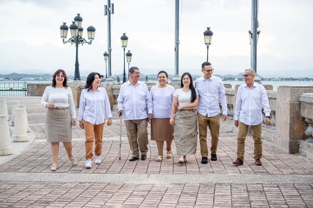 Group photo of people in coordinated white and beige outfits on seaside promenade.