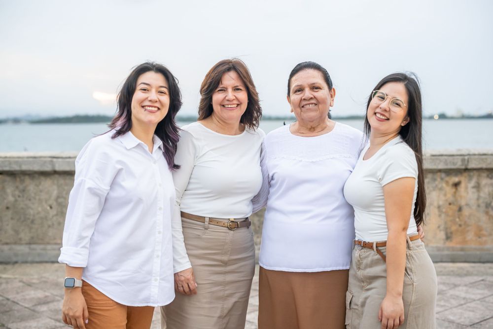 Four people in coordinating white and neutral outfits pose together by a waterfront.