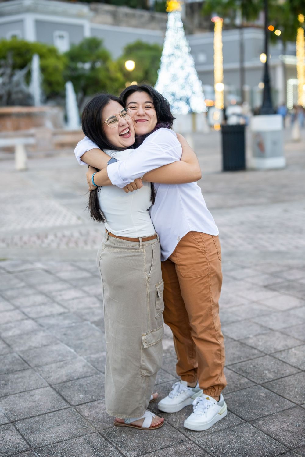 Two people share a warm embrace while laughing on a stone plaza.