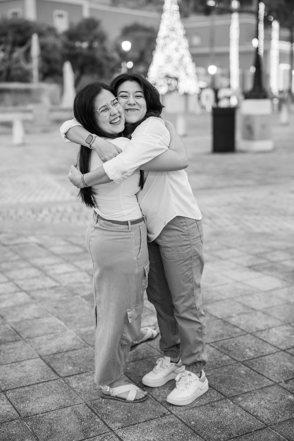 Black and white photo of two people embracing and laughing outdoors.