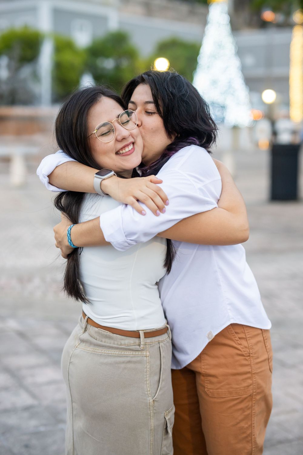 Two people share an affectionate moment with holiday lights twinkling in the background.
