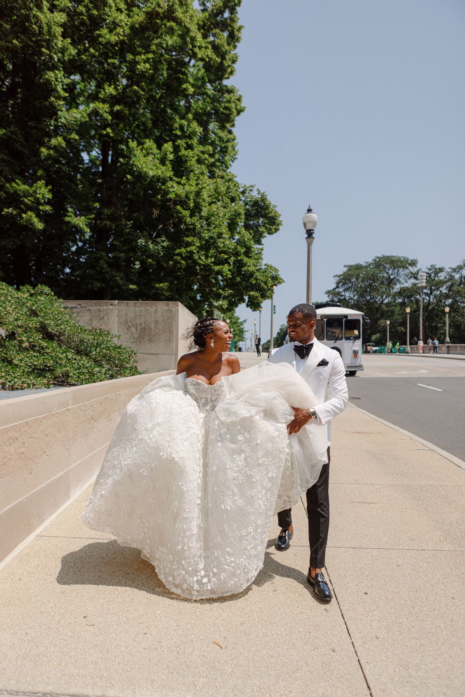 Wedding couple playfully handling a large bubble wrap roll on a city sidewalk.