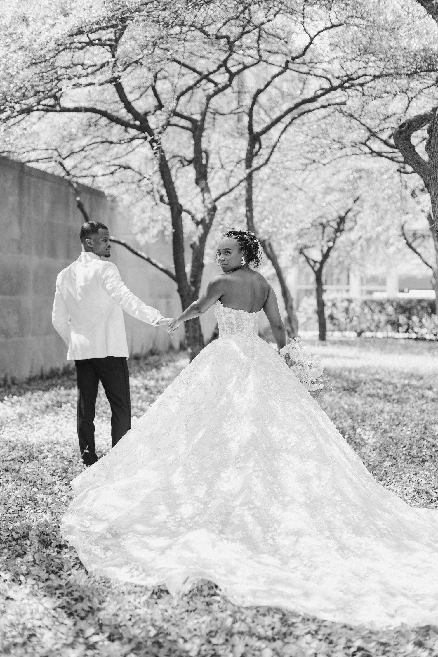 Elegant wedding couple poses under blooming trees in black and white photography.
