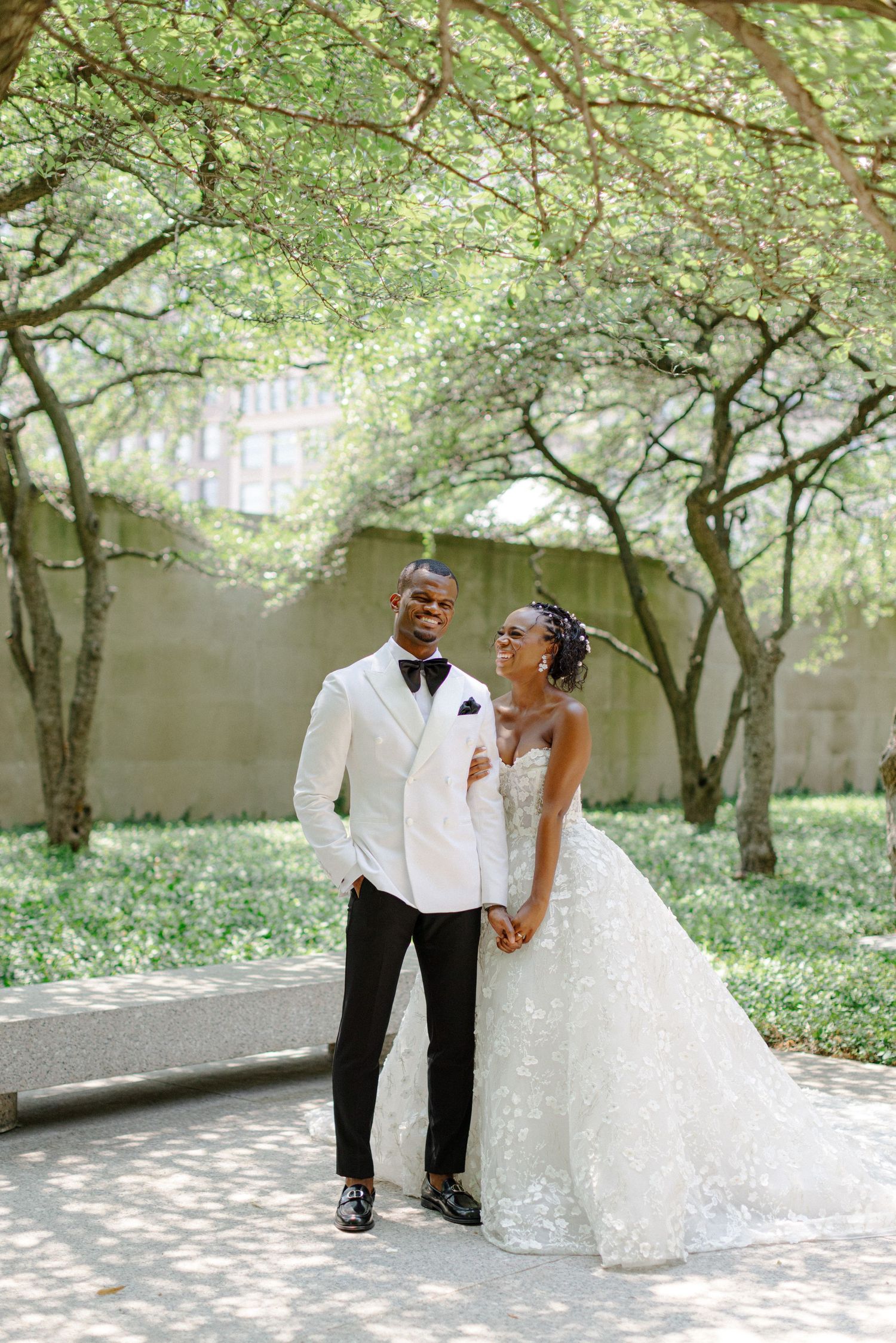 Joyful wedding couple laughing together in urban garden setting.