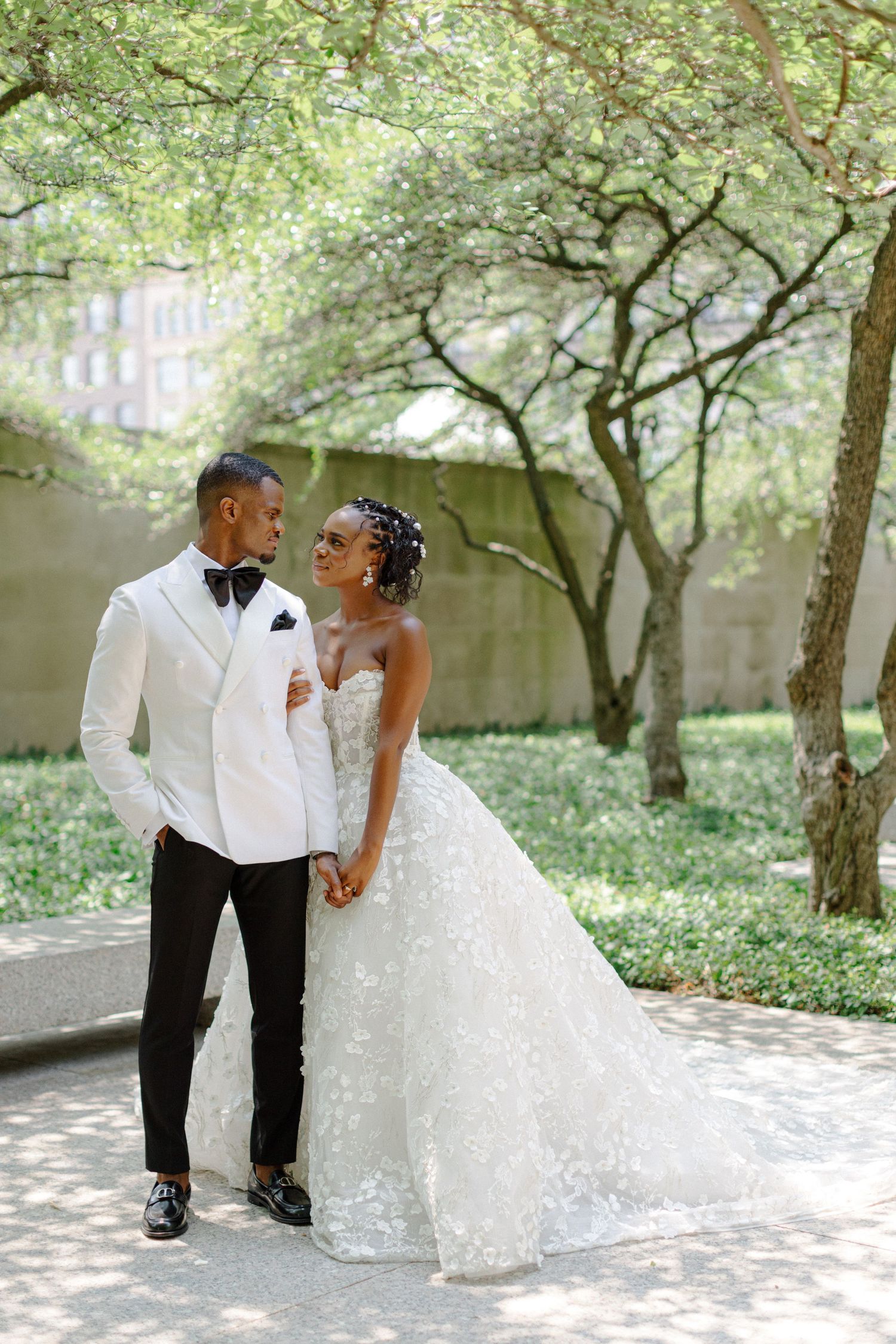 Elegant couple poses on garden path with bride in stunning lace gown.