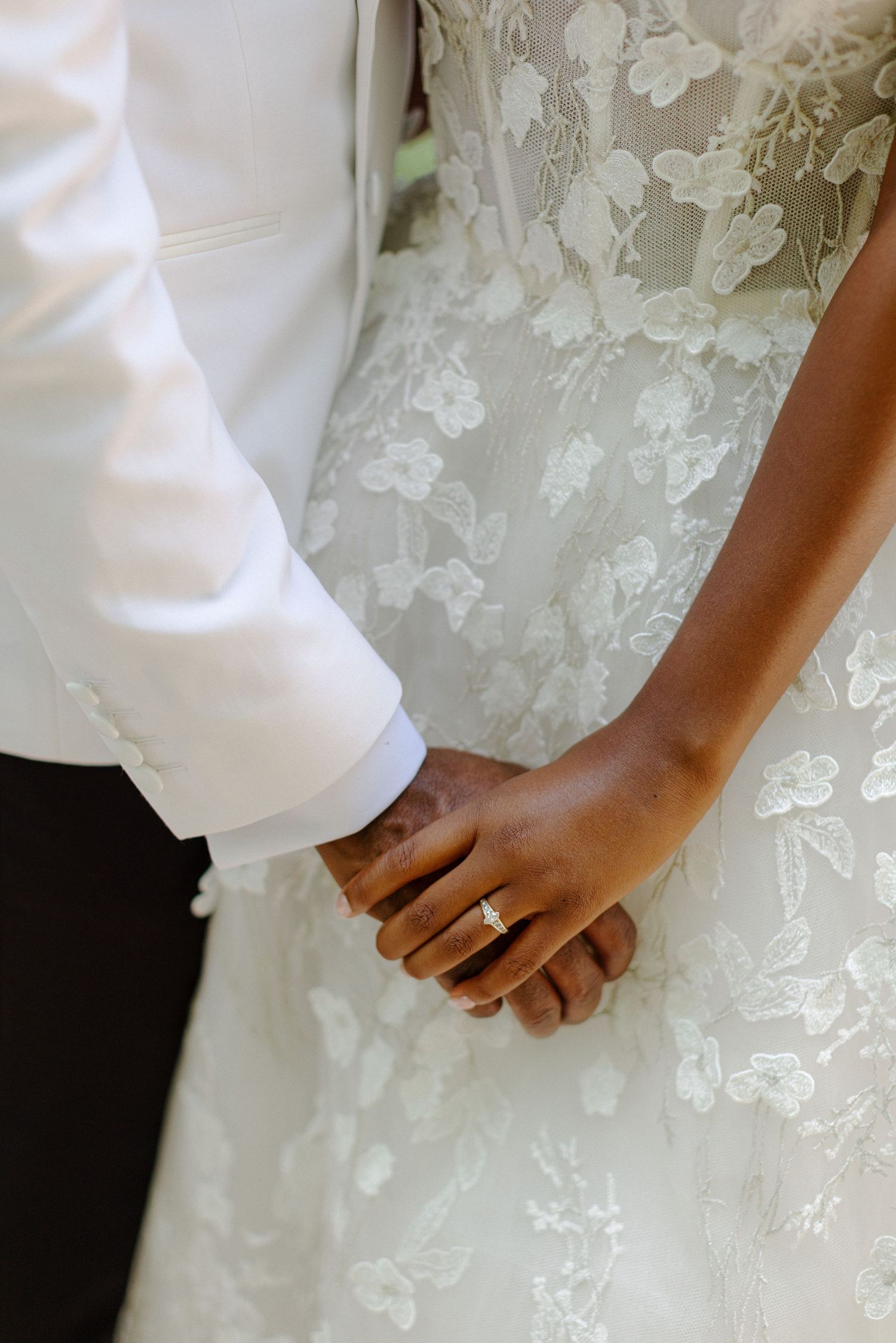 Close-up of newlyweds holding hands showing wedding ring and lace details.