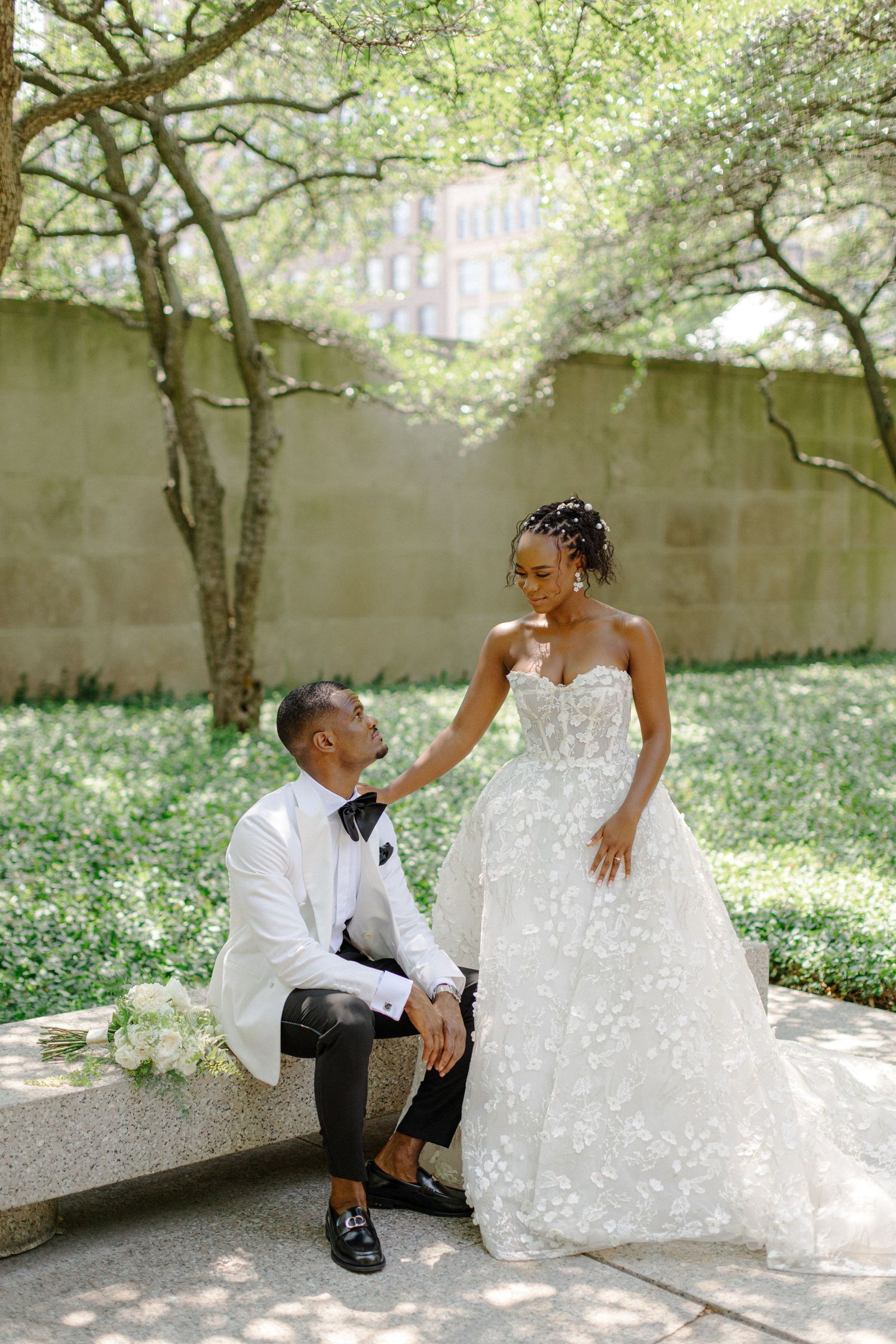 A tender wedding moment captured in a garden setting with stone walls.